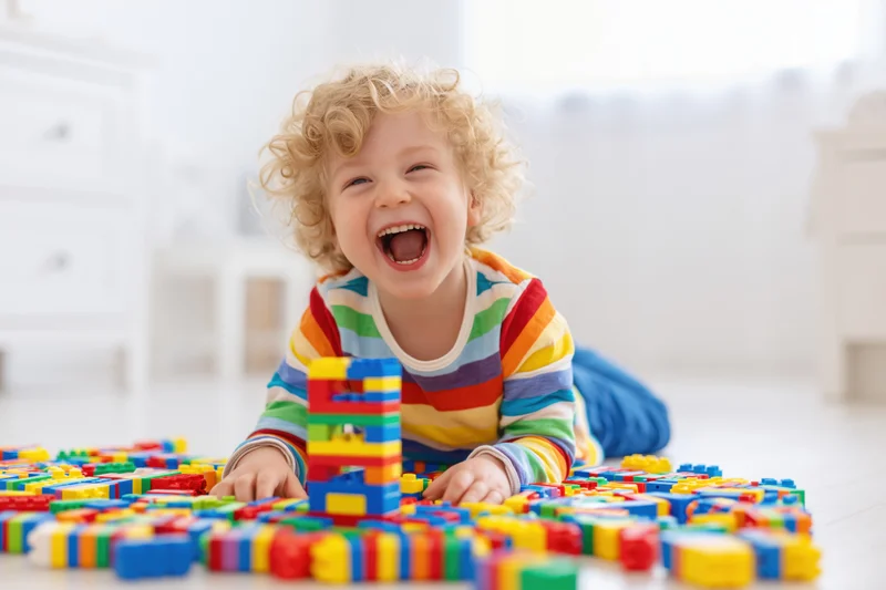 Curly blond toddler laughing while playing with colorful building blocks on the floor