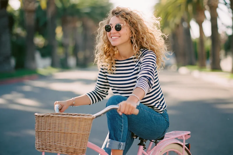 Woman riding a pink vintage bicycle with a wicker basket in a palm-lined park