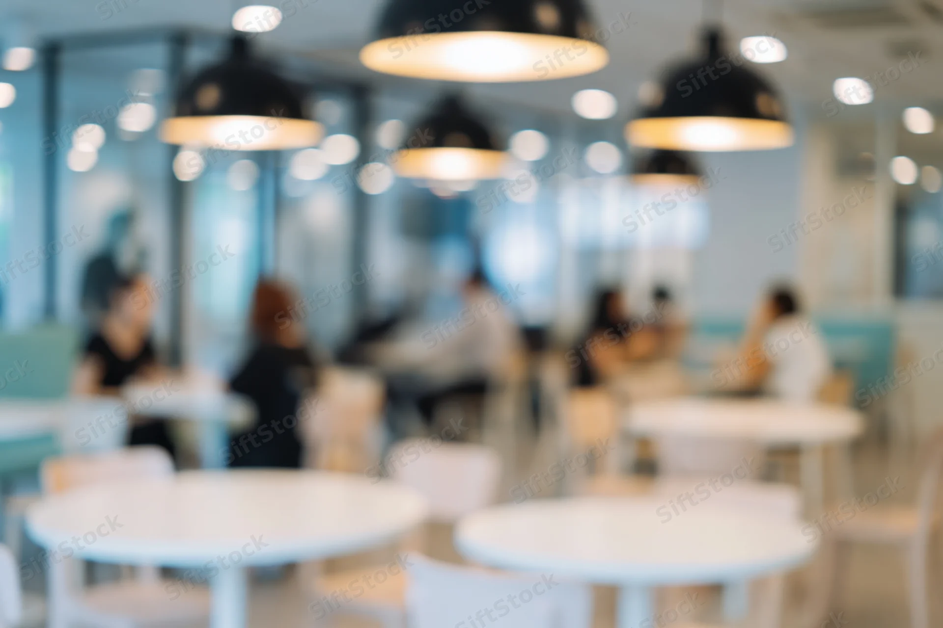 Blurred interior of a modern cafe with seated patrons and pendant lights above white tables