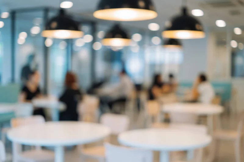 Blurred interior of a modern cafe with seated patrons and pendant lights above white tables