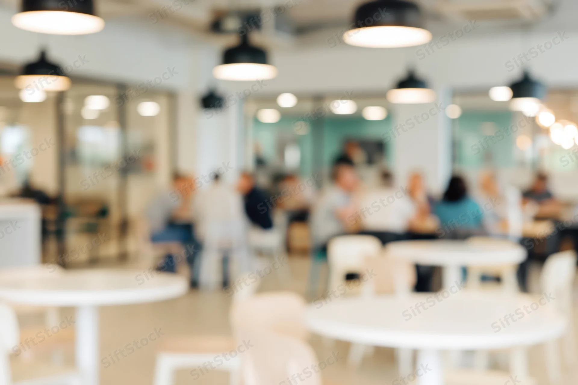 Defocused interior of a modern cafe with seated patrons and white tables under pendant lights