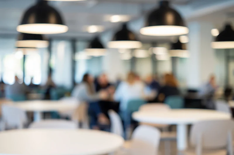 Defocused interior of a modern cafe with seated patrons and round tables under pendant lights