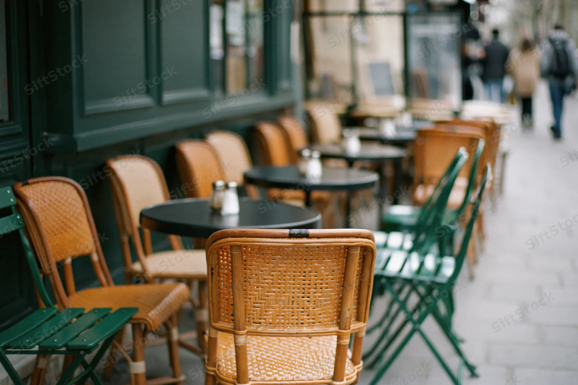 Empty parisian cafe terrace with small round black bistro tables and wicker chairs along the sidewalk