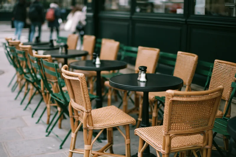Empty parisian cafe terrace with round black tables and wicker chairs arranged along the sidewalk