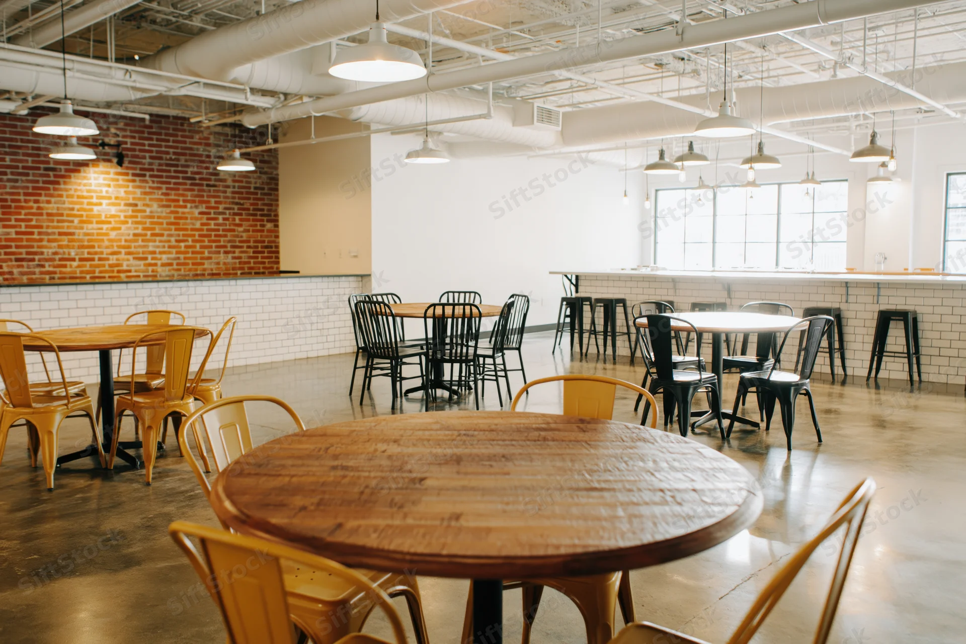 Empty industrial-style cafe interior with round wooden tables and metal chairs arranged on concrete floor