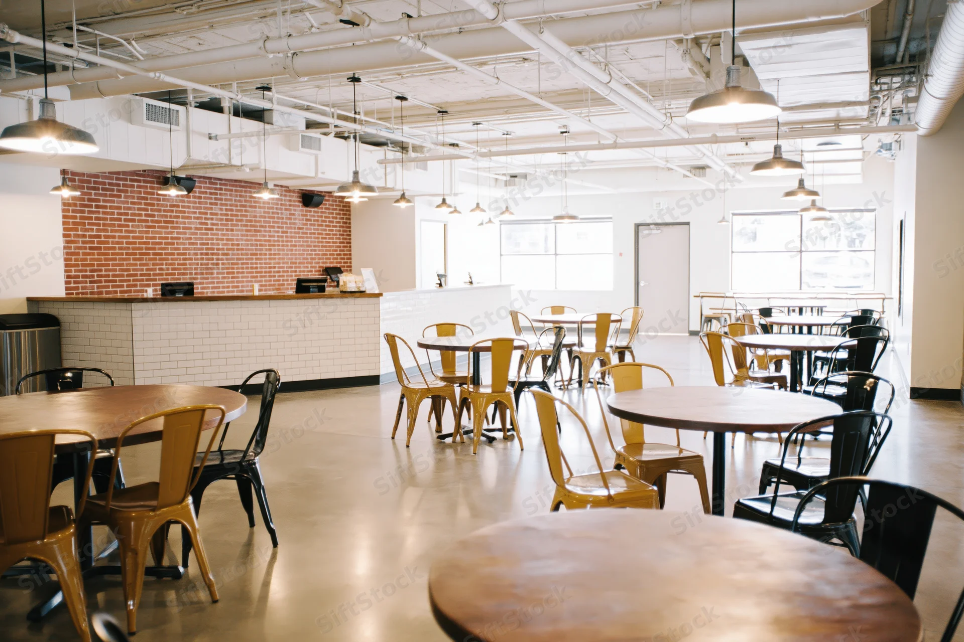Empty industrial-style cafe interior with round wooden tables and metal chairs arranged in open space