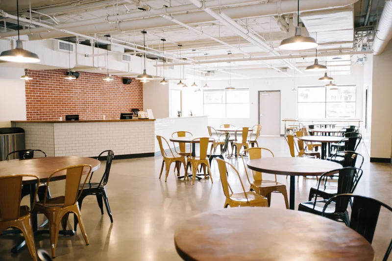 Empty industrial-style cafe interior with round wooden tables and metal chairs arranged in open space