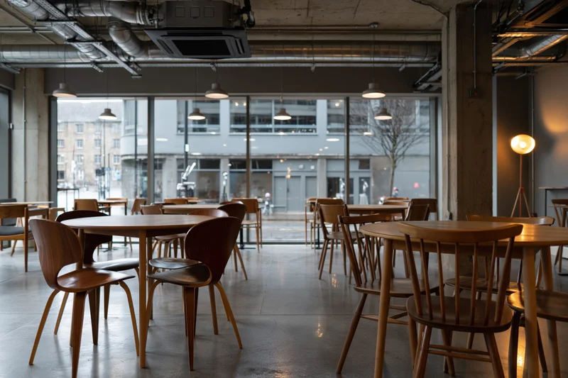 Empty industrial-style cafe interior with wooden round tables and large windows overlooking the street