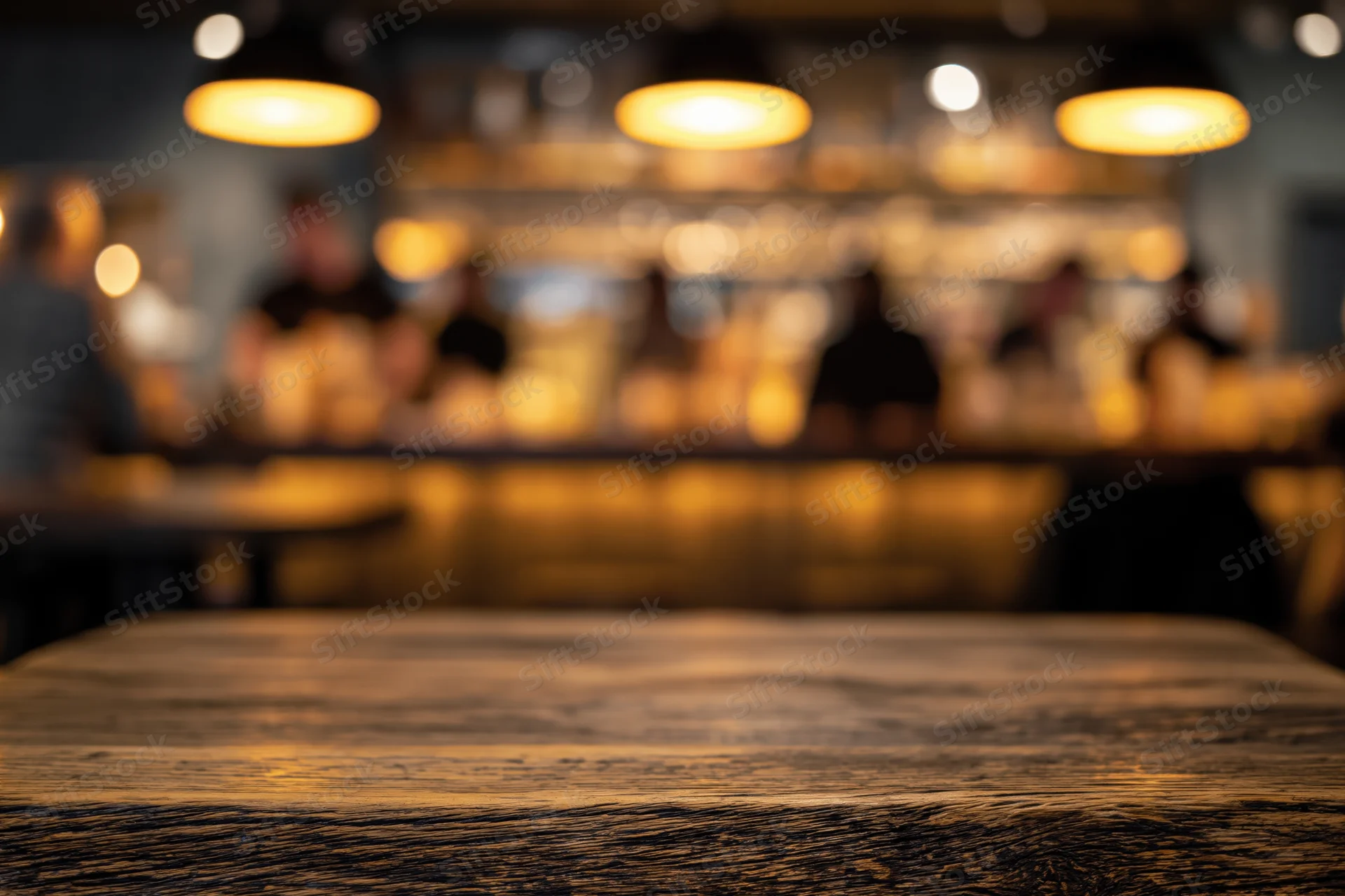 Rustic wooden table surface in foreground with blurred bar and patrons in background