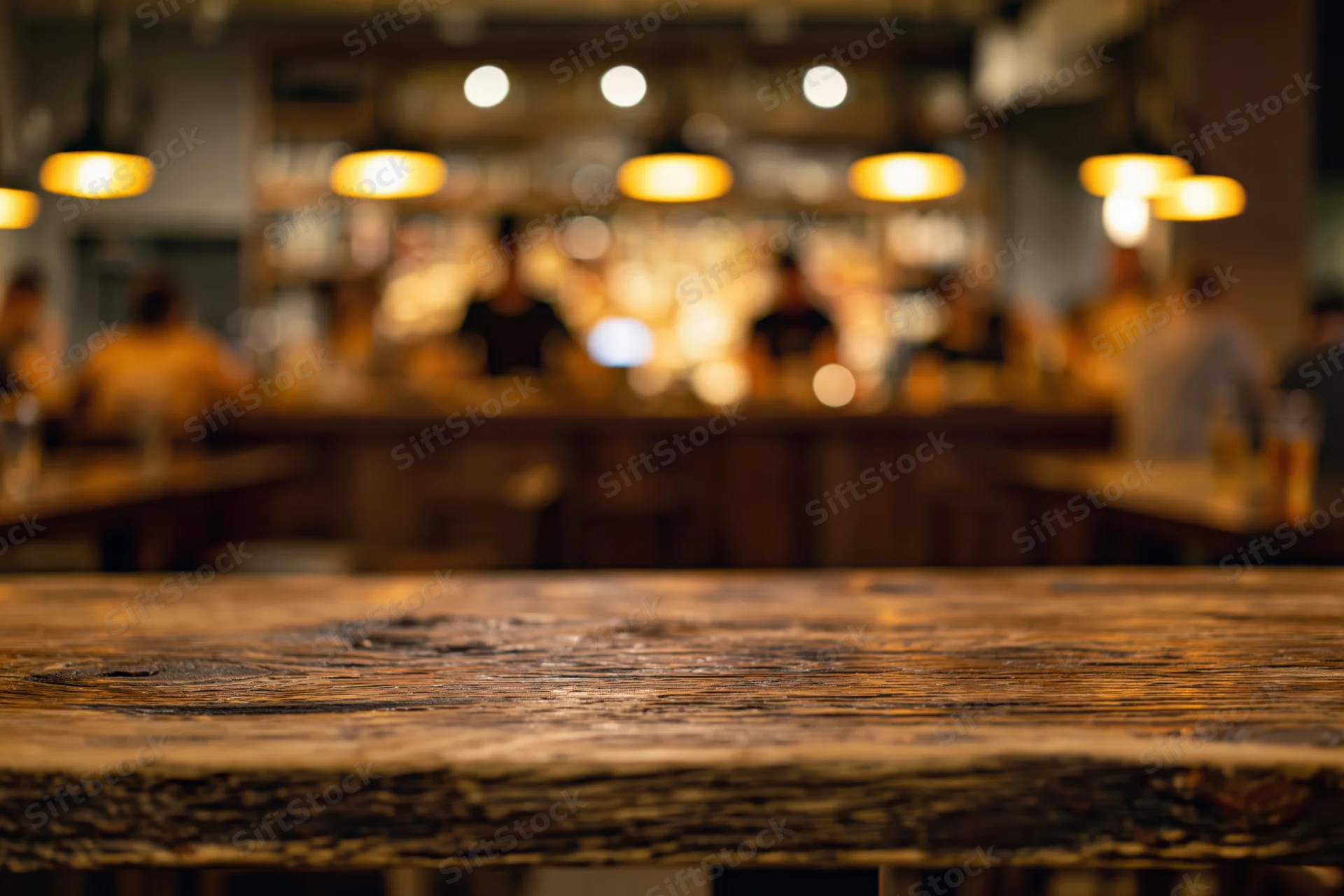 Rustic wooden table surface in foreground with blurred bar interior and warm pendant lights in background
