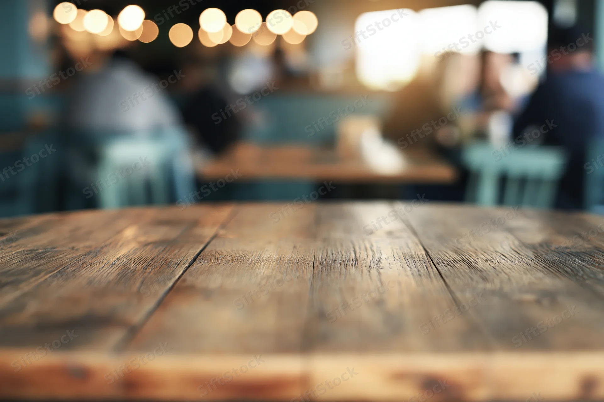 Empty rustic wooden table in foreground of blurred cafe interior with patrons and warm lighting