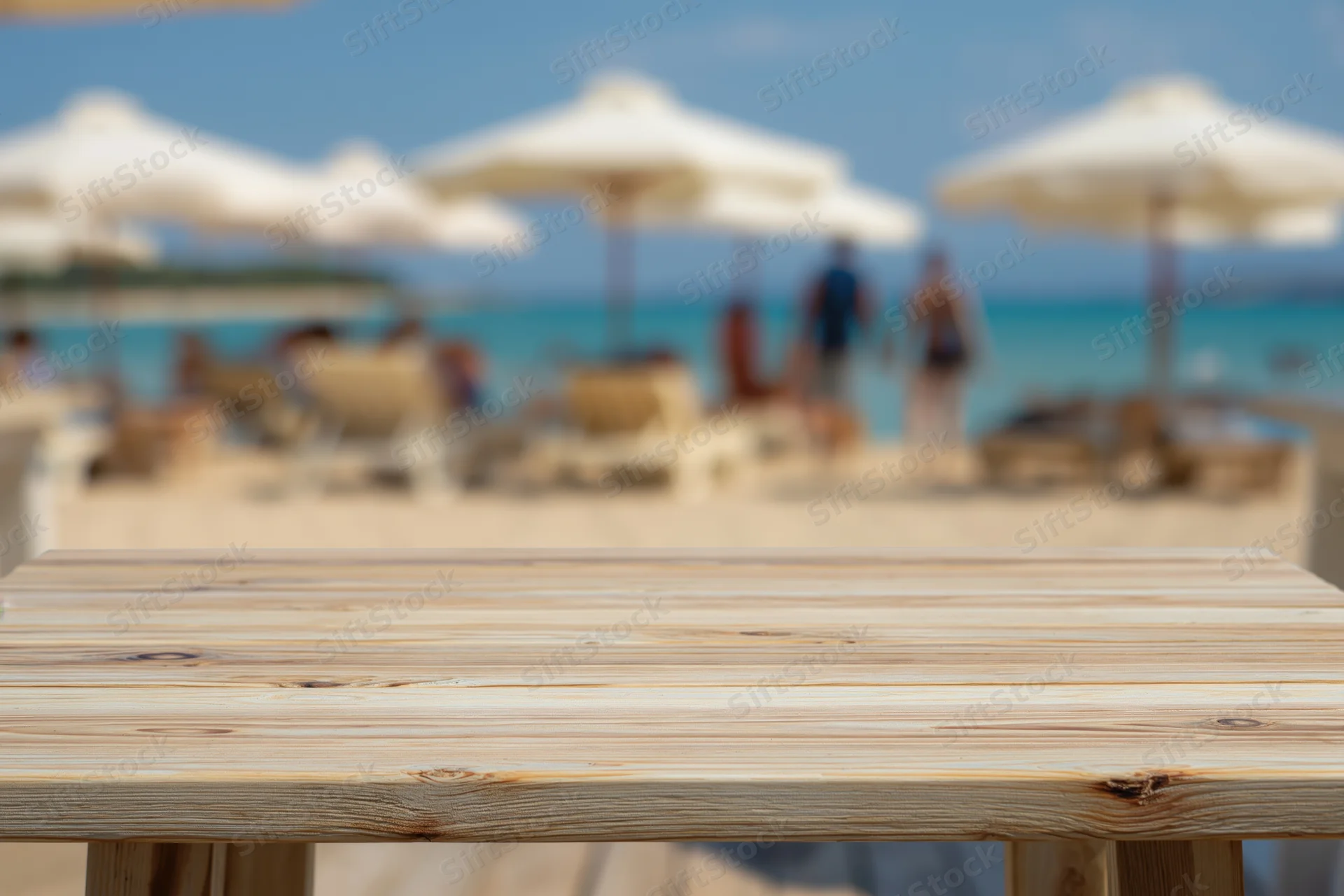 Wooden table top in sharp focus with blurred beach and umbrellas in background