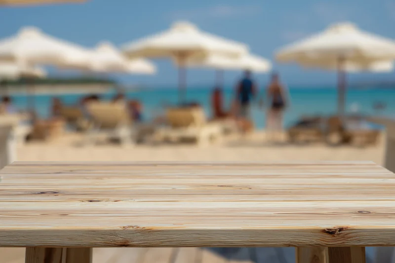 Wooden table top in sharp focus with blurred beach and umbrellas in background