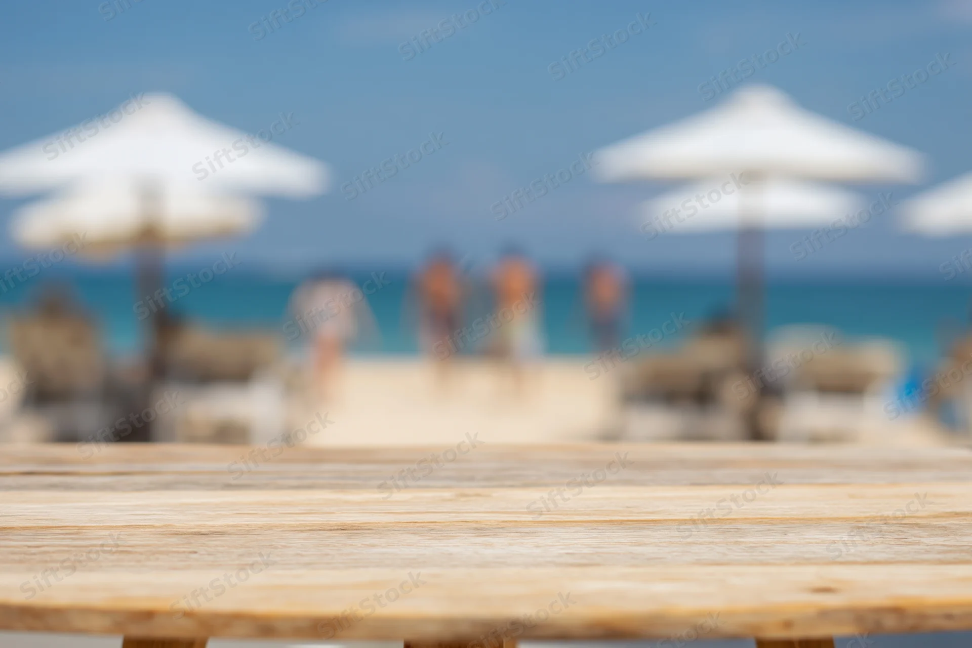 Wooden table in sharp focus with blurred beach and umbrellas in background