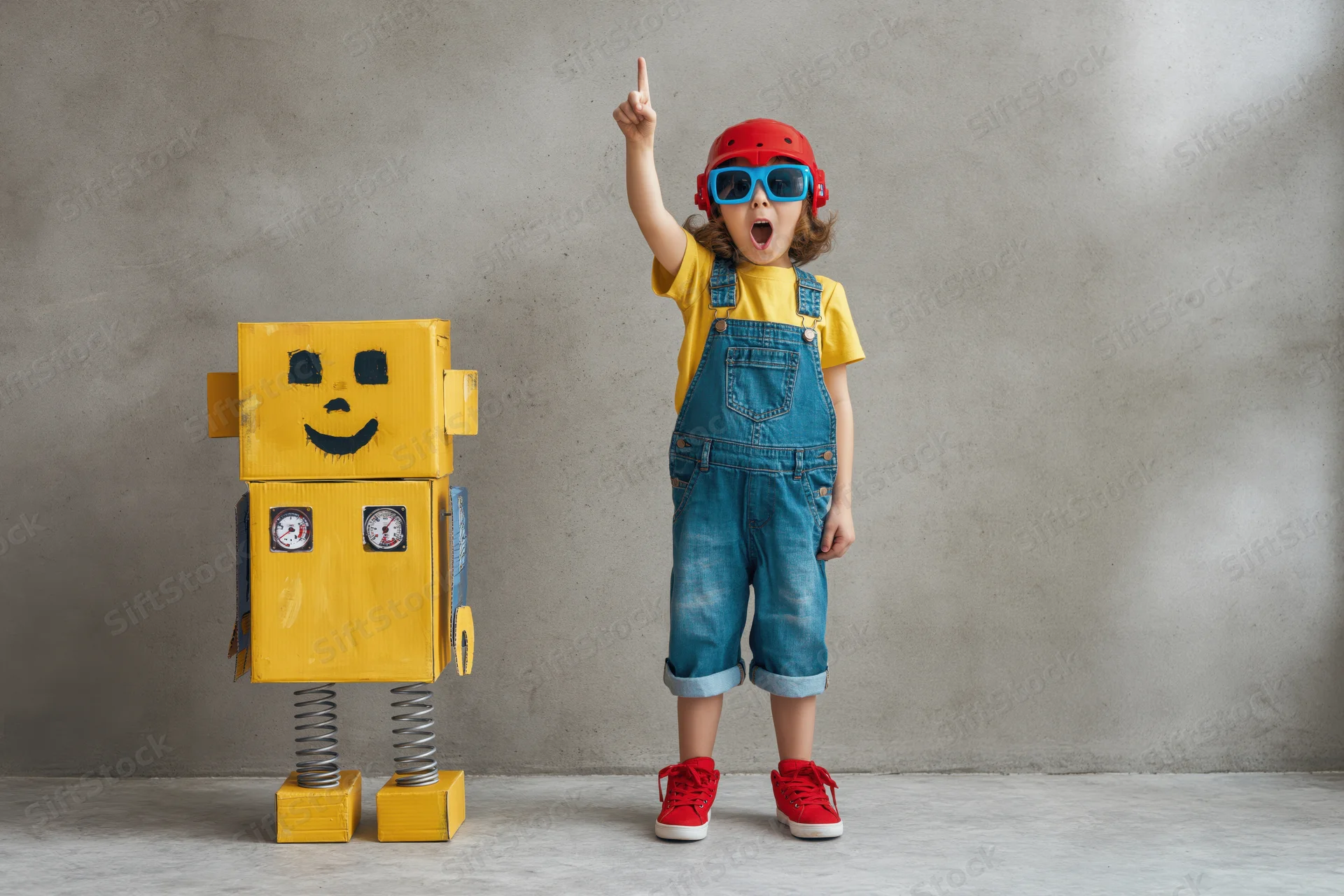 Excited child pointing upward while standing next to a homemade yellow cardboard robot indoors
