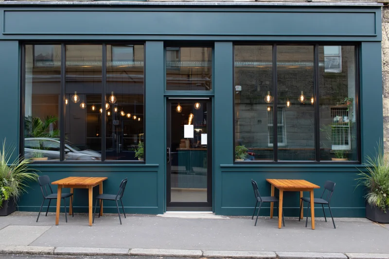 Modern cafe exterior with teal facade and outdoor seating on sidewalk
