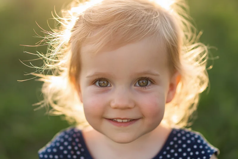 Close-up portrait of a smiling blonde toddler girl outdoors in golden hour light