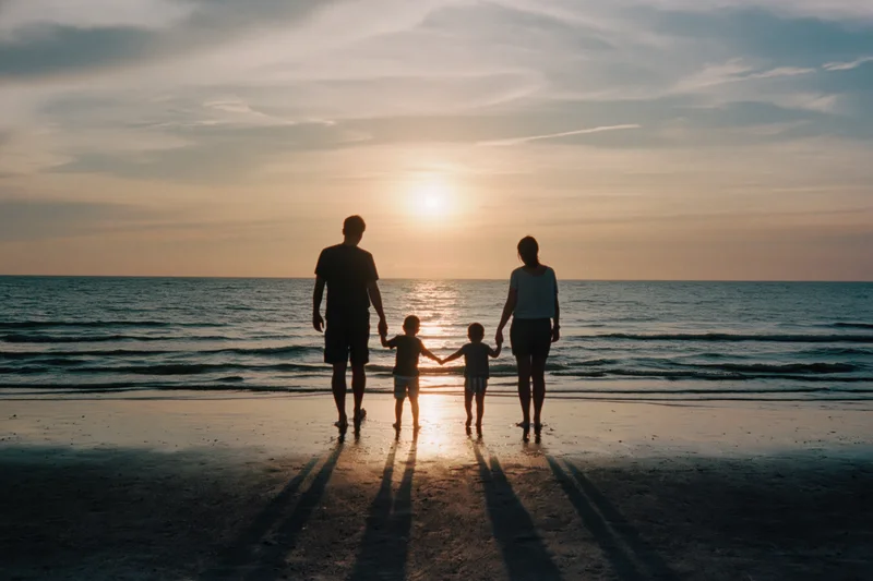 Family of four holding hands walking toward ocean at sunset on beach