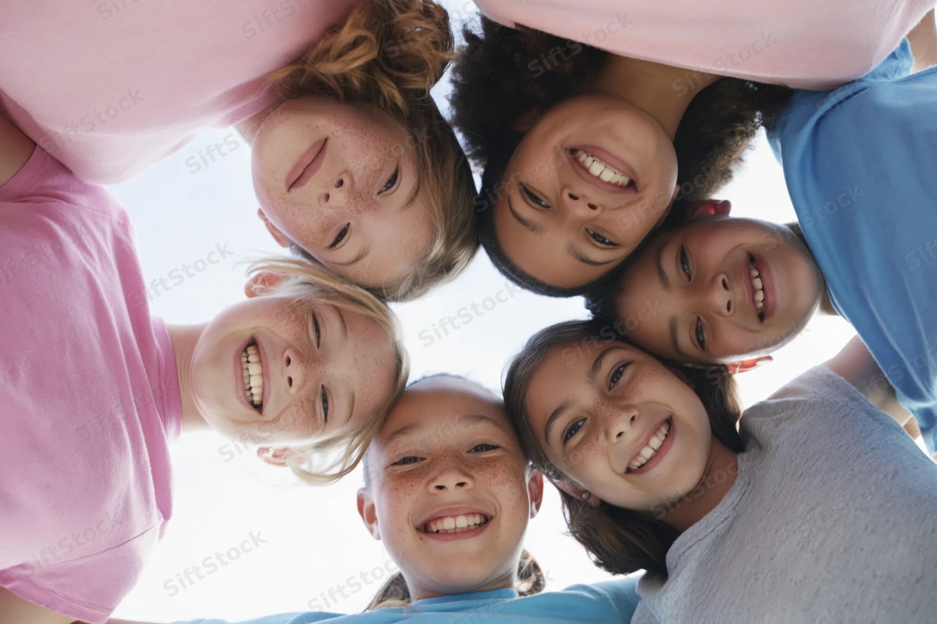 Five children of different ethnicities huddled in a circle smiling down at the camera from above