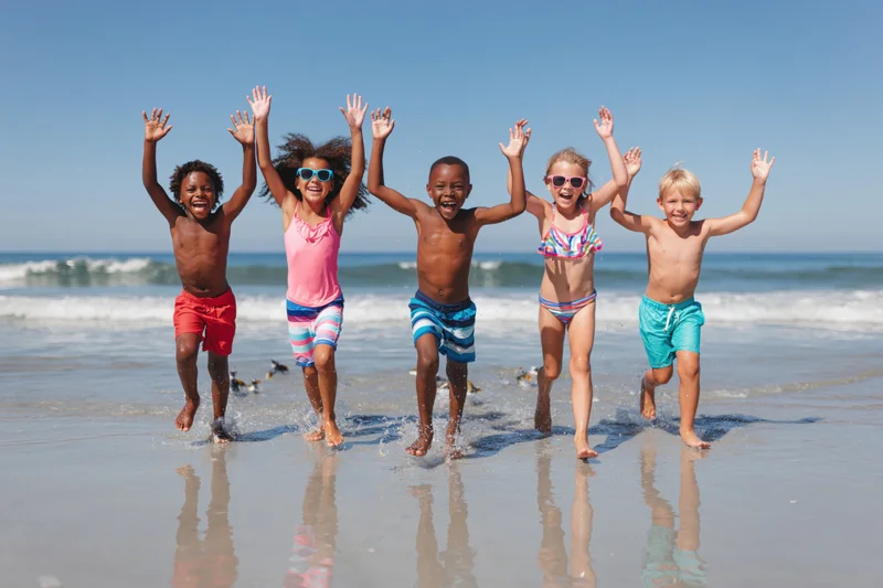 Five diverse children running joyfully along the wet sand at the beach