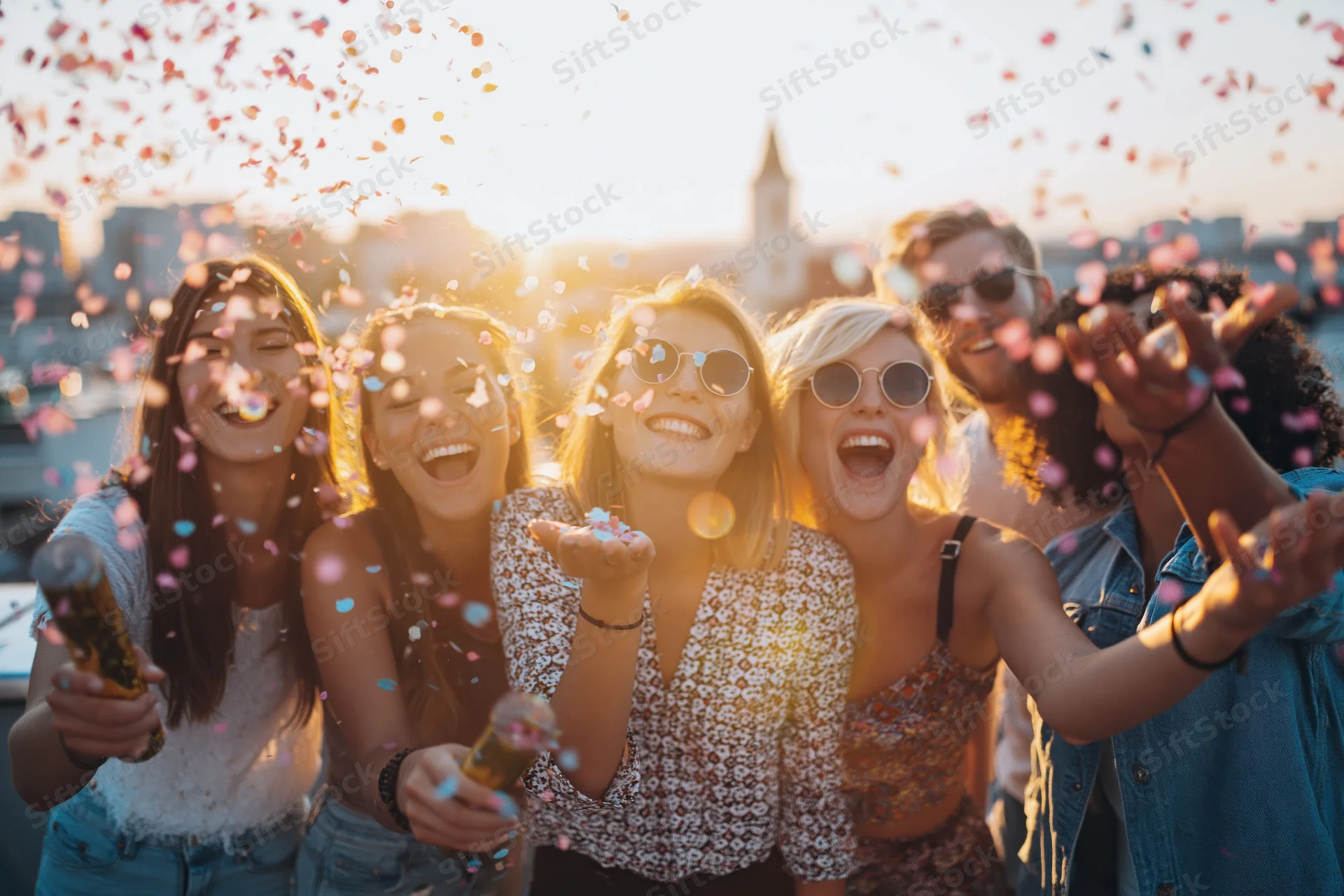Young friends laughing and throwing confetti on a rooftop at sunset