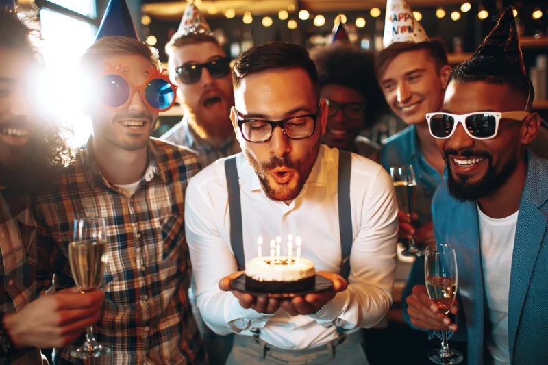 Man blowing out candles on birthday cake surrounded by friends in a bar