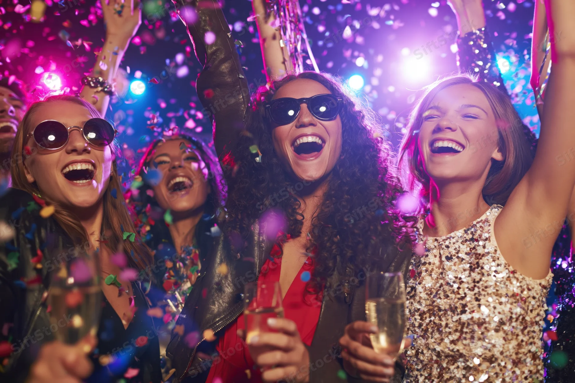 Young women laughing and dancing with arms raised at a nightclub party