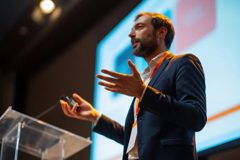 Man speaking at podium gesturing during presentation at conference
