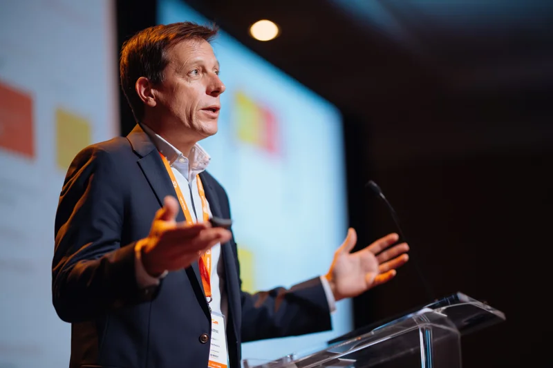 Male speaker gesturing with both hands at podium during presentation on stage