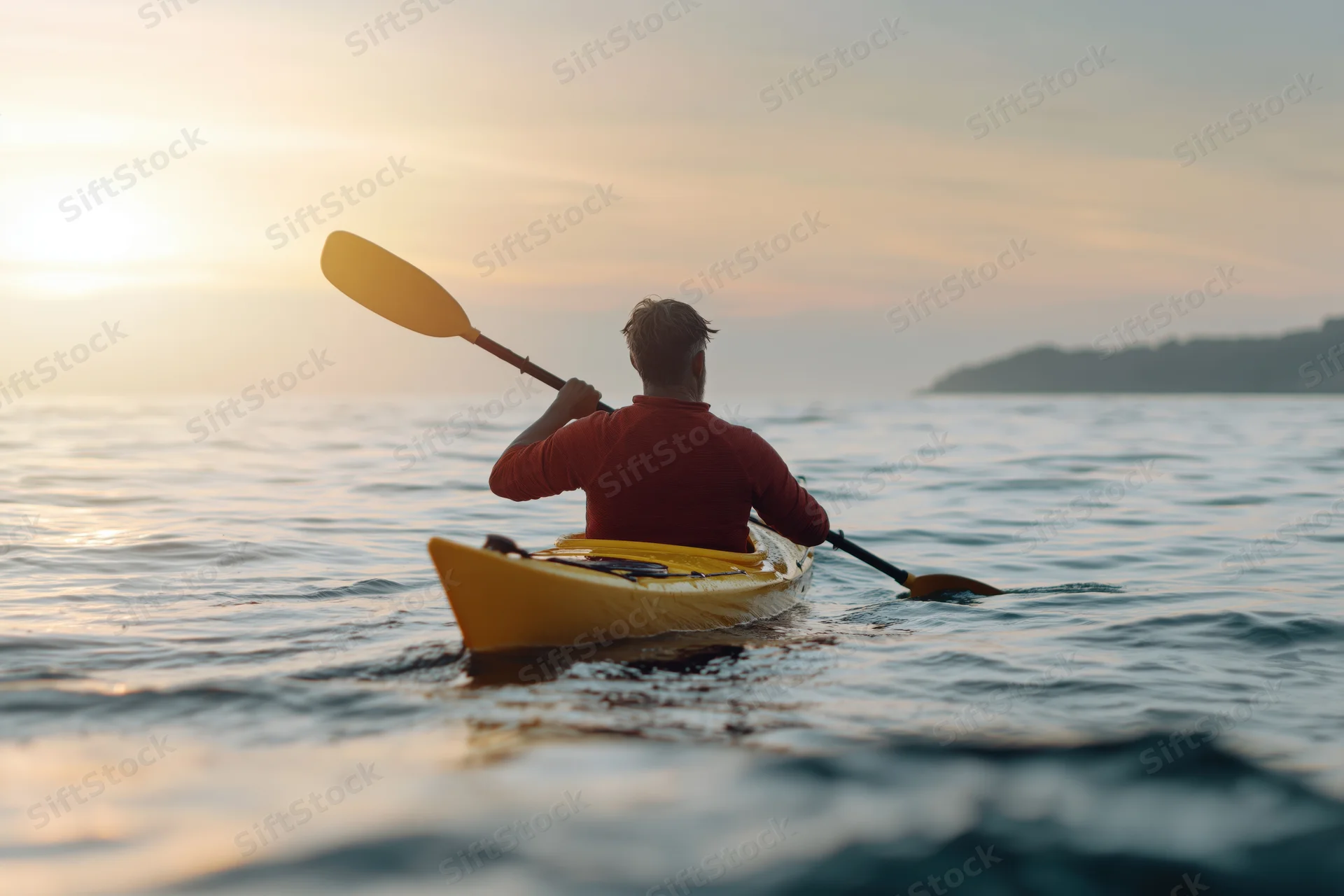 Man paddling a yellow kayak on calm coastal water at sunset