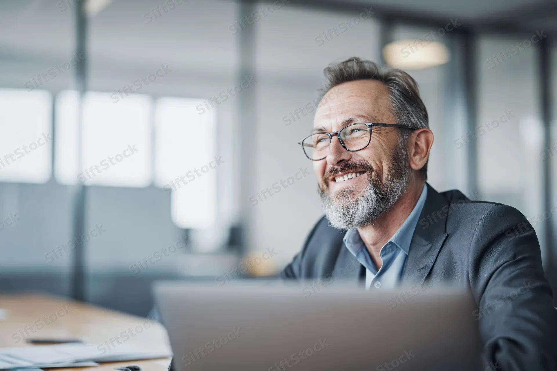 Middle-aged businessman smiling while working on laptop in modern office