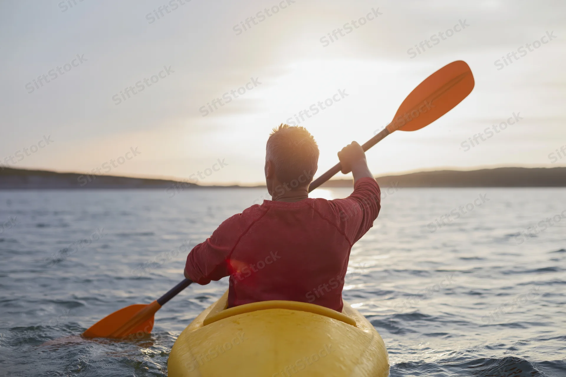 Man paddling a yellow kayak on calm water at sunset