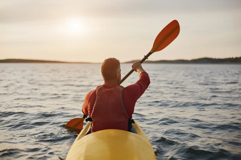 Man paddling a yellow kayak on calm water at sunset