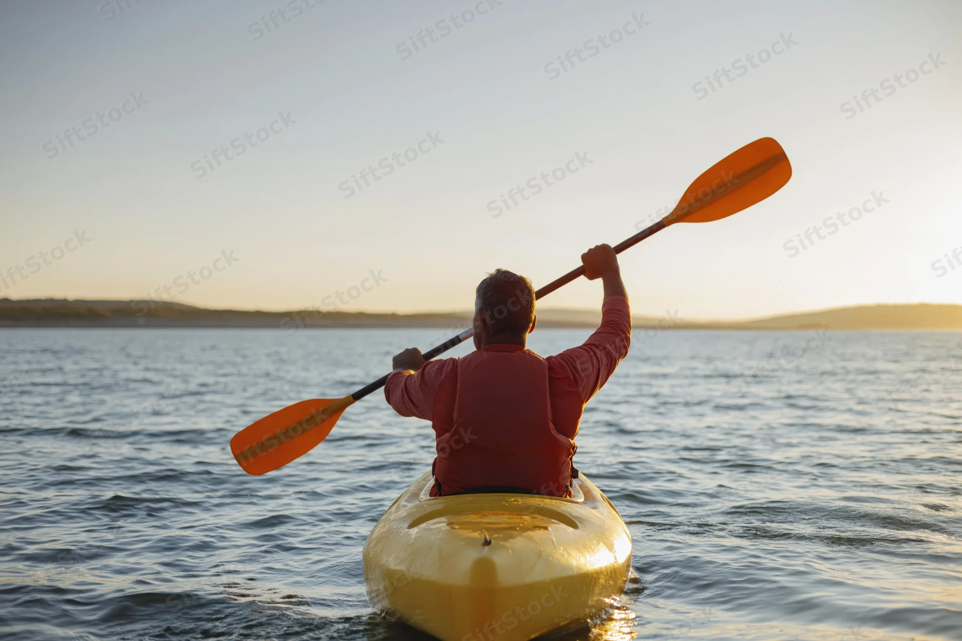 Man paddling a yellow kayak on calm water at sunset