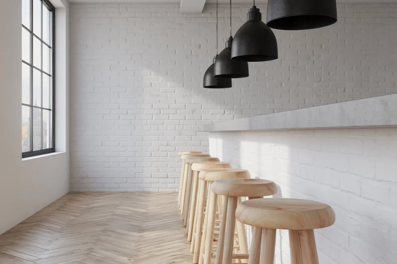 Modern minimalist bar interior with white brick walls, wooden stools, and black pendant lights along a counter
