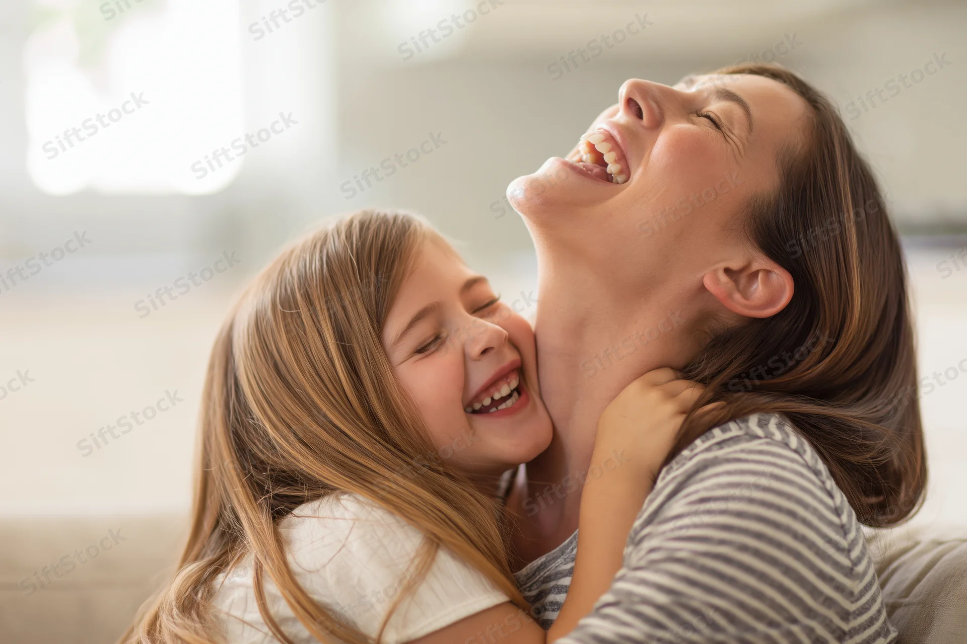Mother and daughter laughing while hugging on a sofa