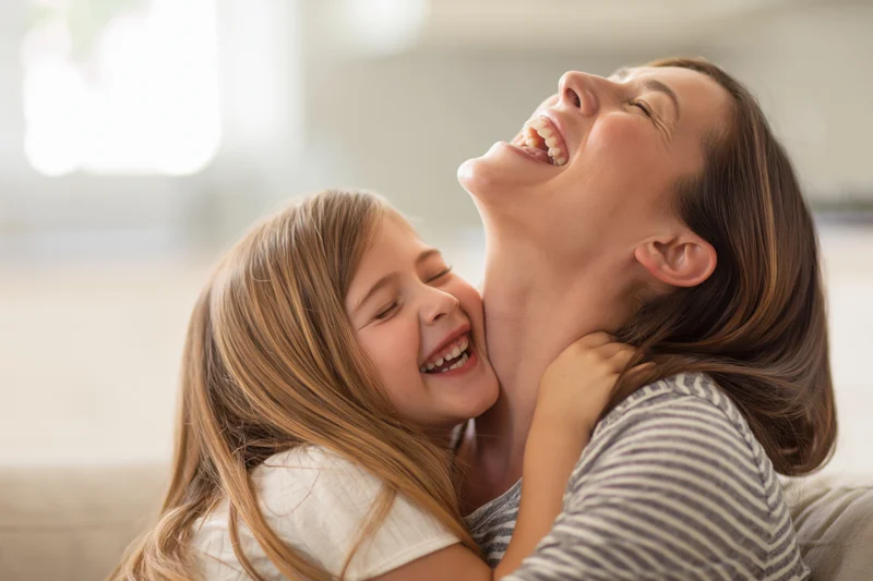 Mother and daughter laughing while hugging on a sofa