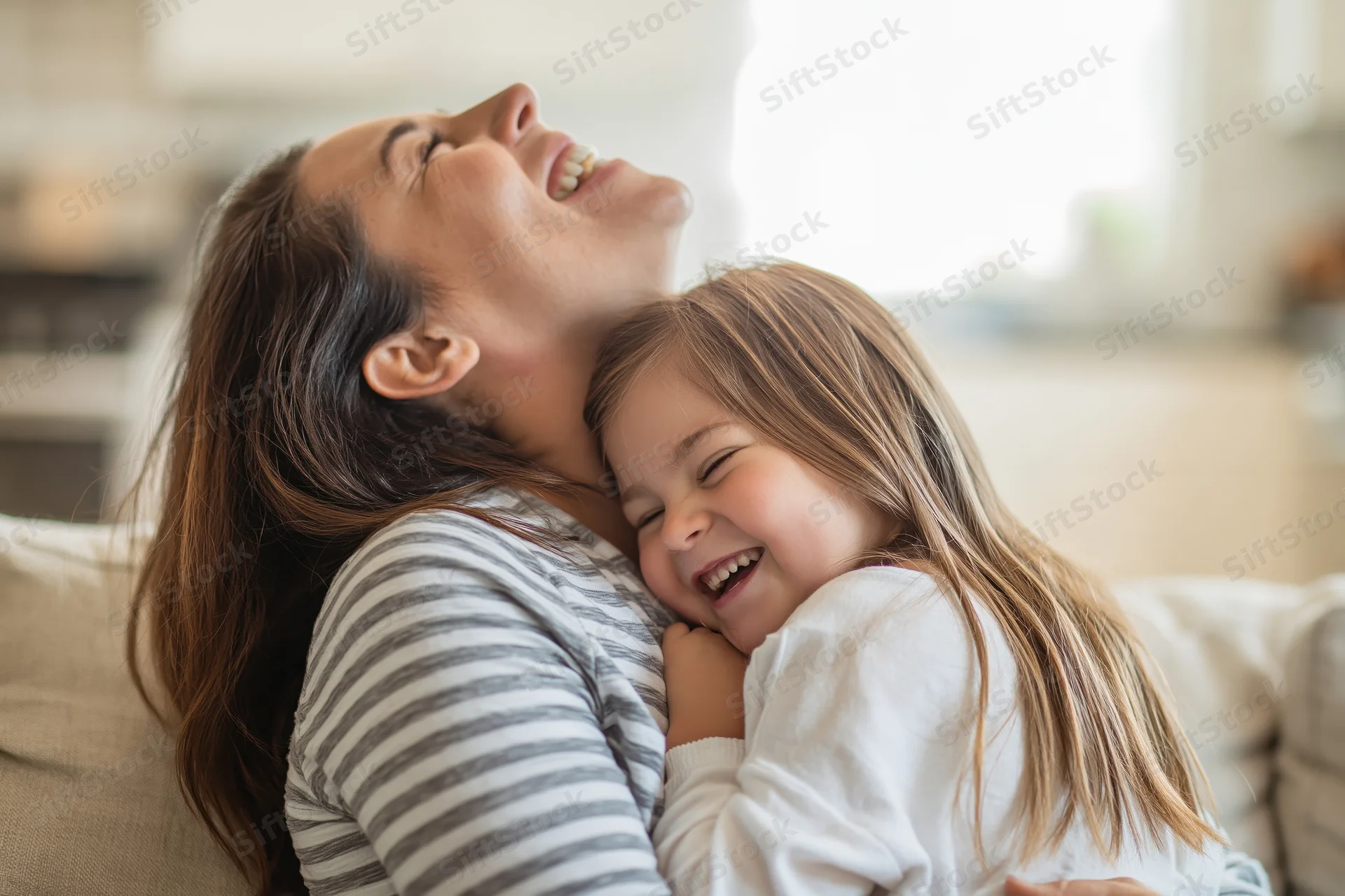 Mother and daughter laughing while hugging on a sofa in a living room