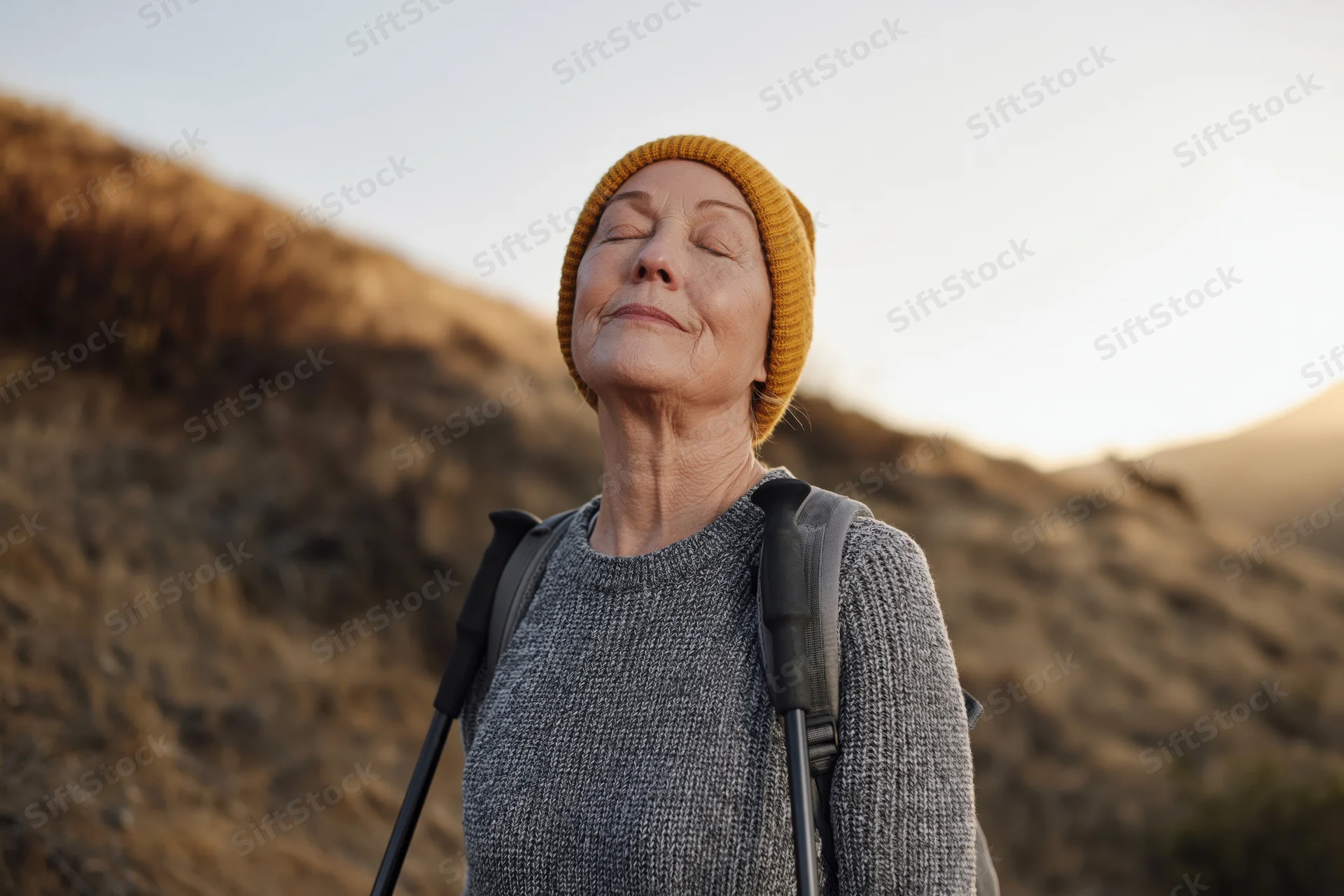 Senior woman with eyes closed and smile hiking in mountains at sunset