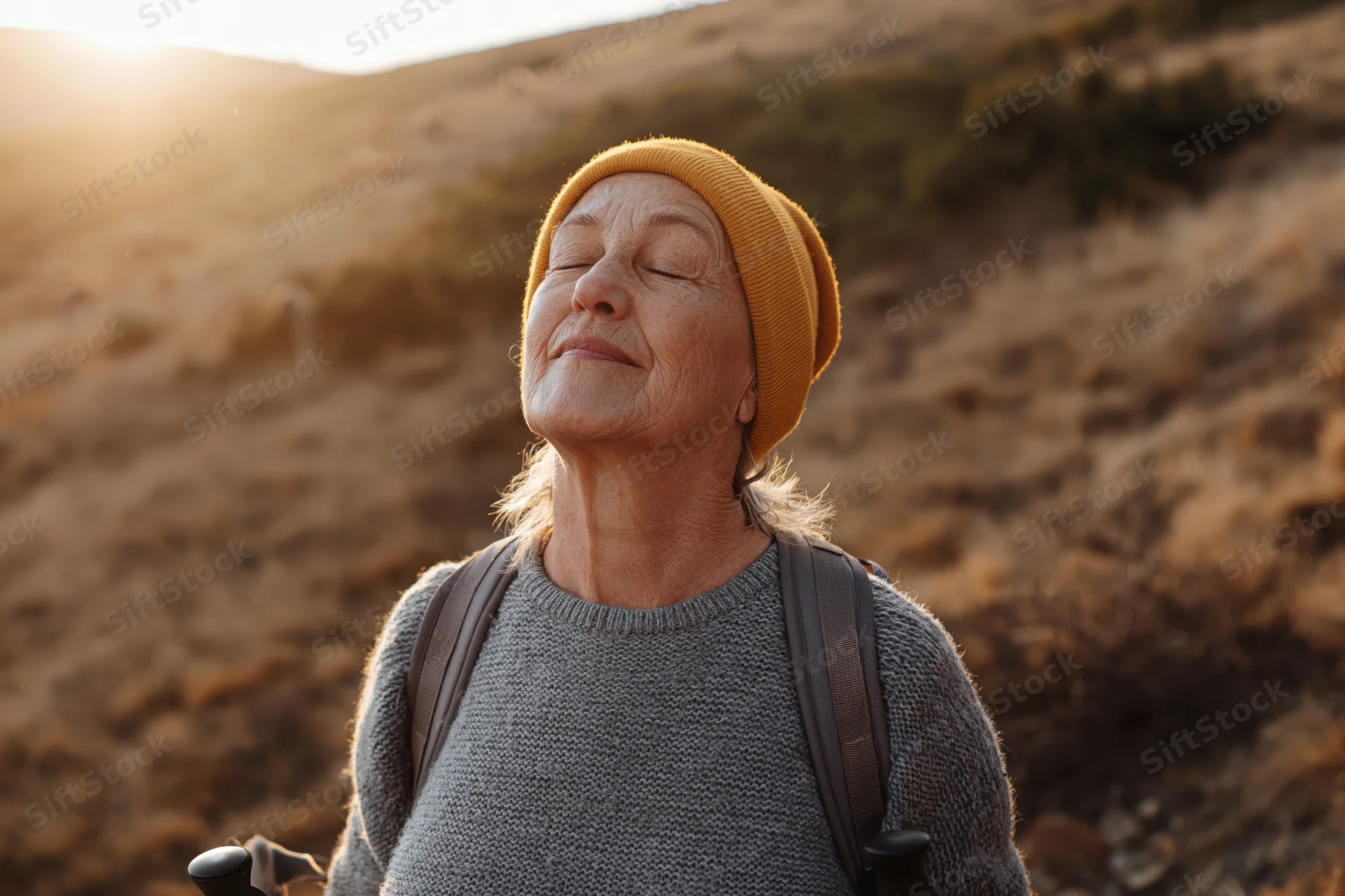 Senior woman with eyes closed and face tilted upward while hiking in a dry hilly landscape at sunset