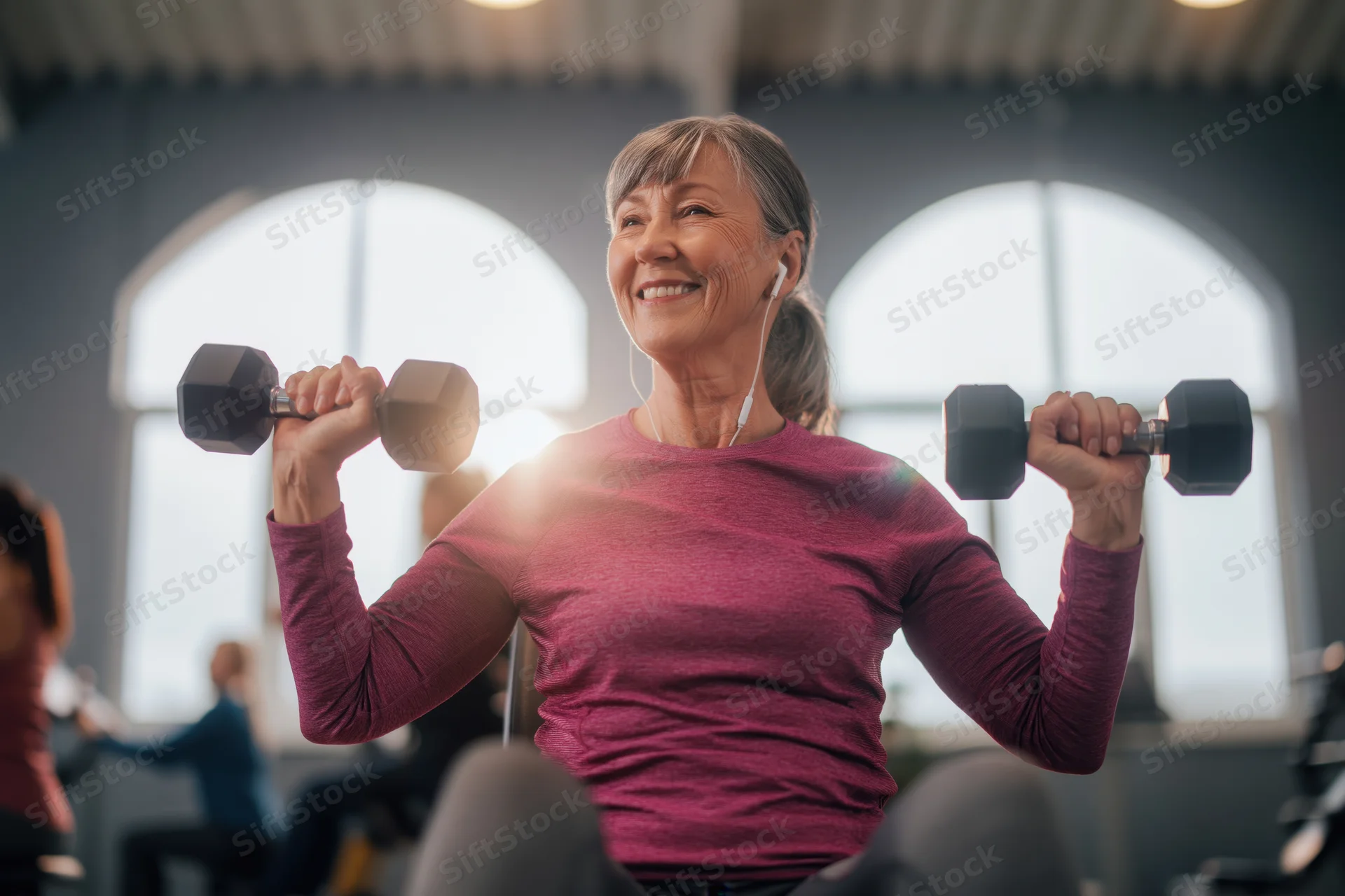 Senior woman smiling while lifting dumbbells in a gym class