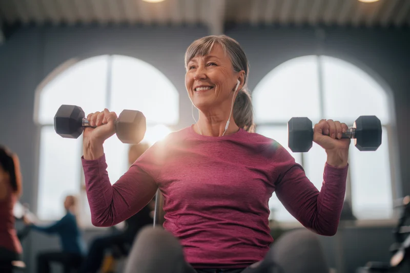 Senior woman smiling while lifting dumbbells in a gym class