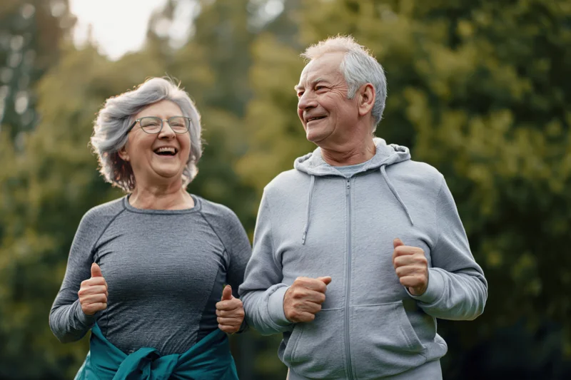 Senior couple jogging midstride in a park smiling and moving together