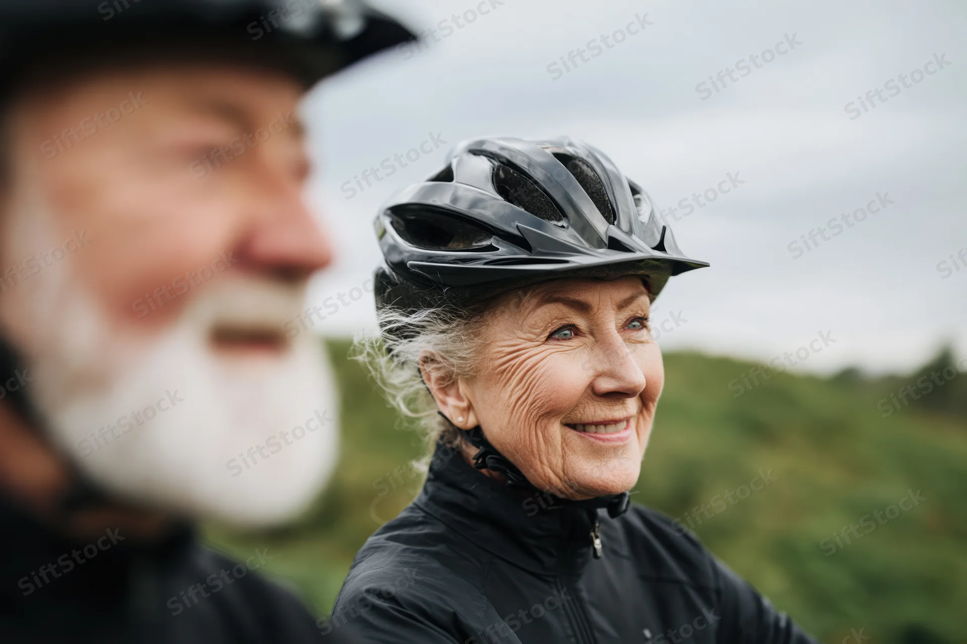 Senior woman wearing bicycle helmet smiling outdoors with man in background
