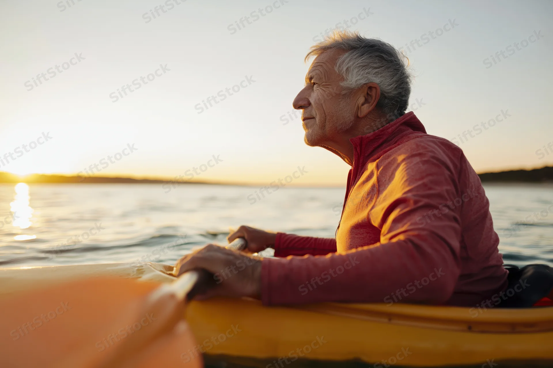 Senior man paddling a yellow kayak on calm water at sunset