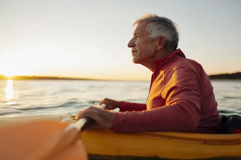 Senior man paddling a yellow kayak on calm water at sunset