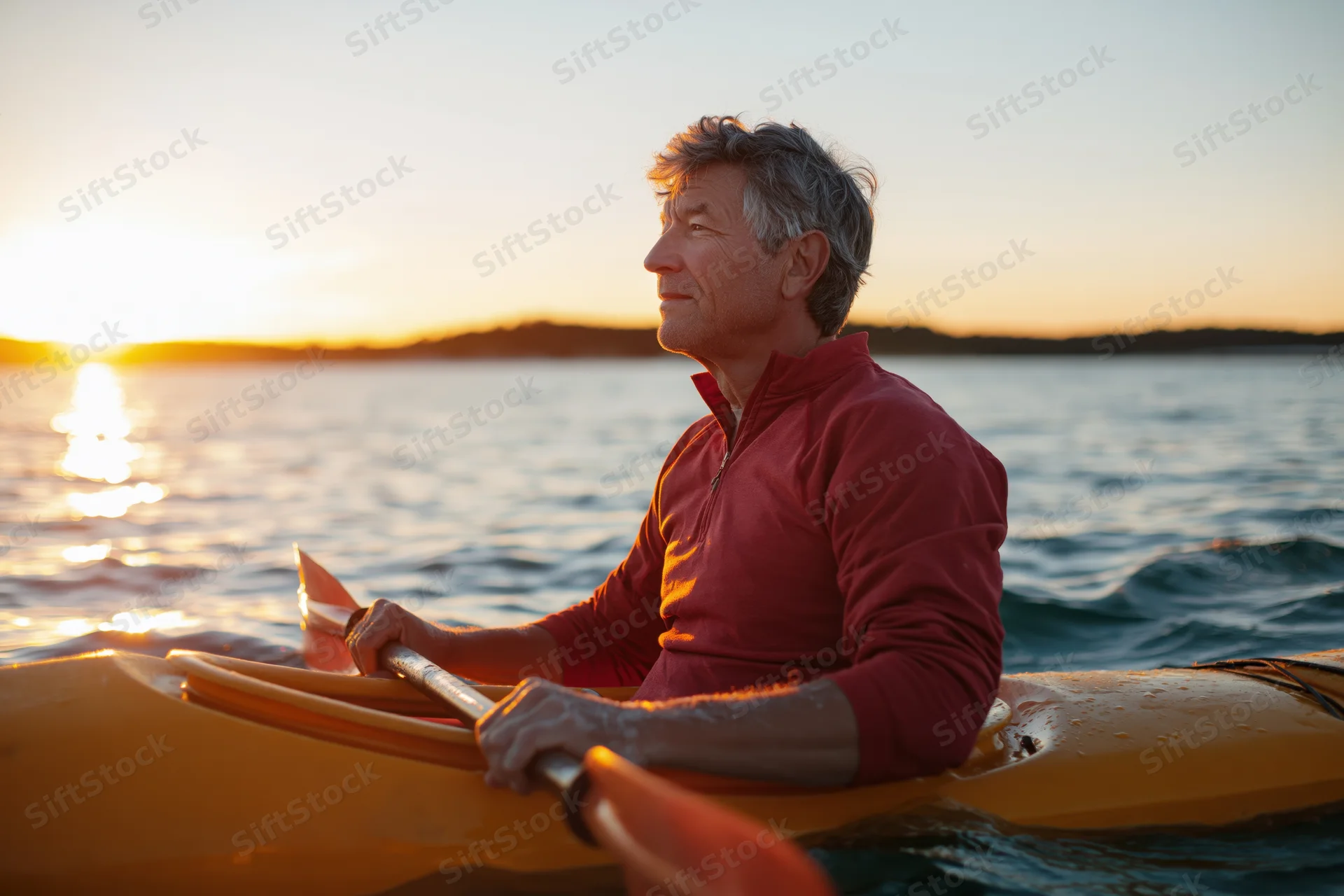 Senior man paddling a yellow kayak on calm water at sunset