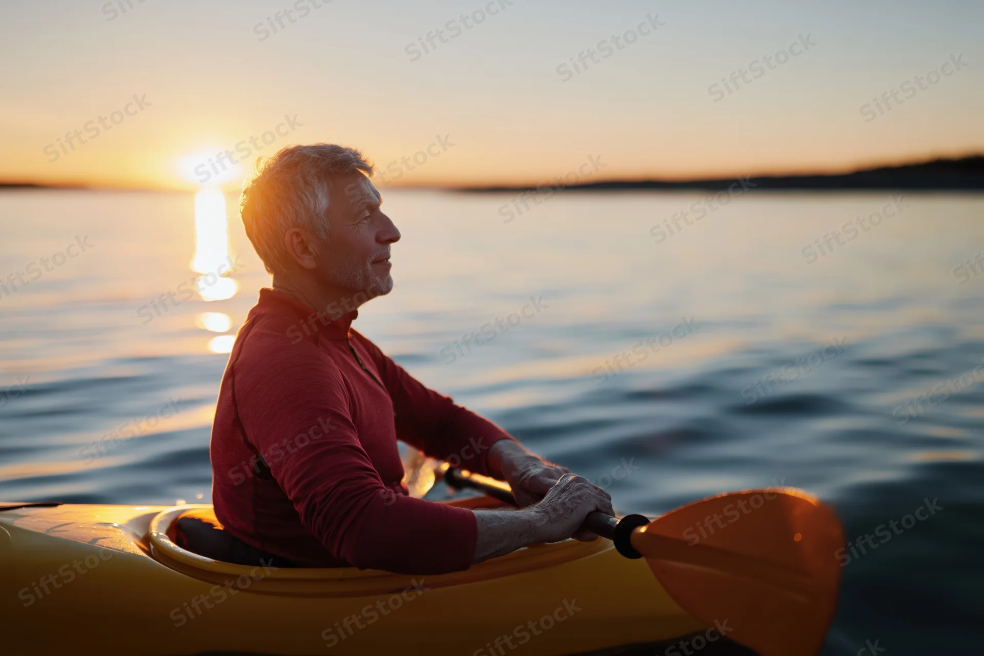 Senior man paddling a yellow kayak on calm water at sunset
