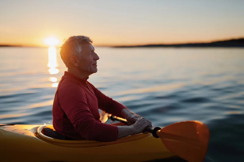 Senior man paddling a yellow kayak on calm water at sunset