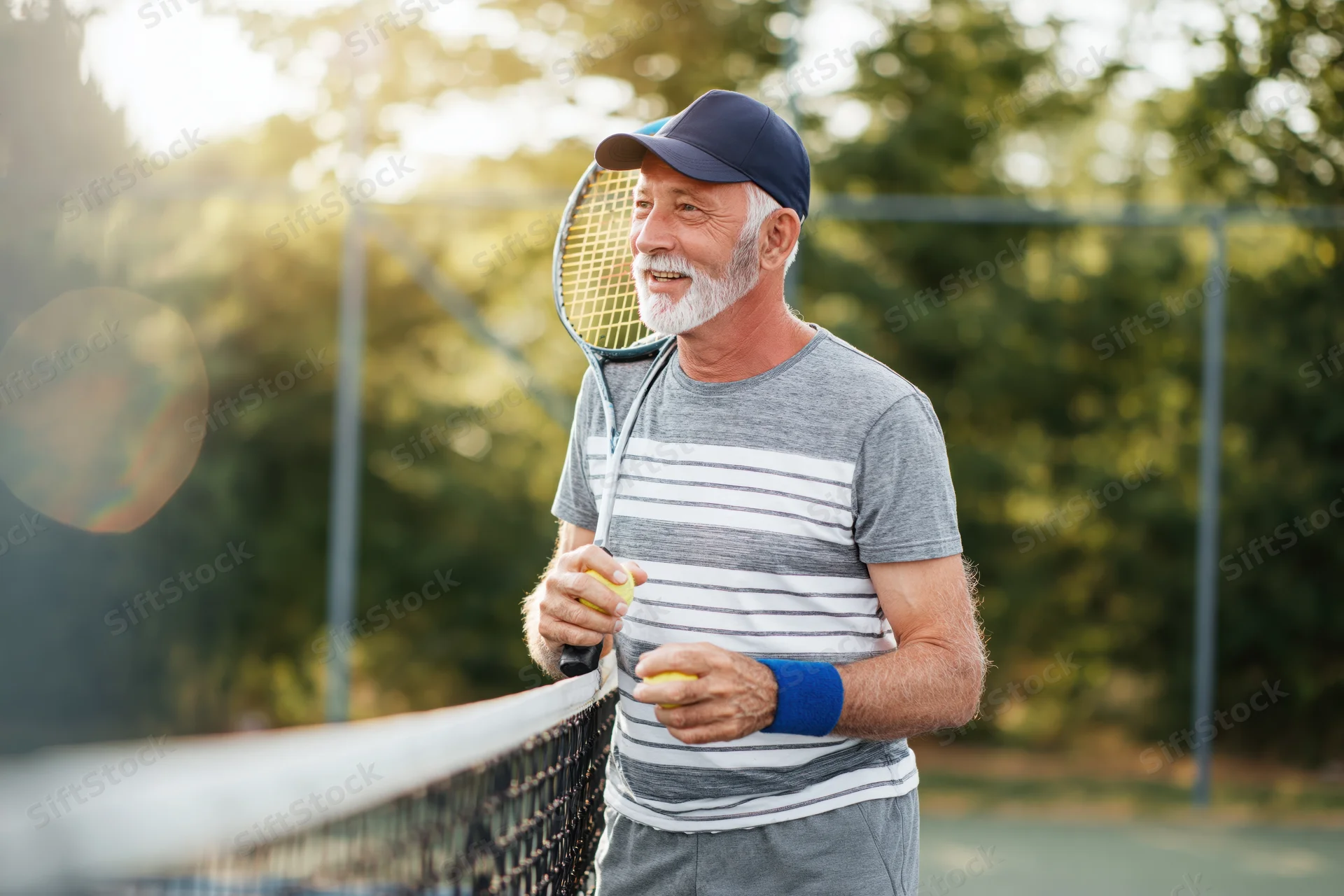 Senior man holding tennis racket and ball by net on outdoor court